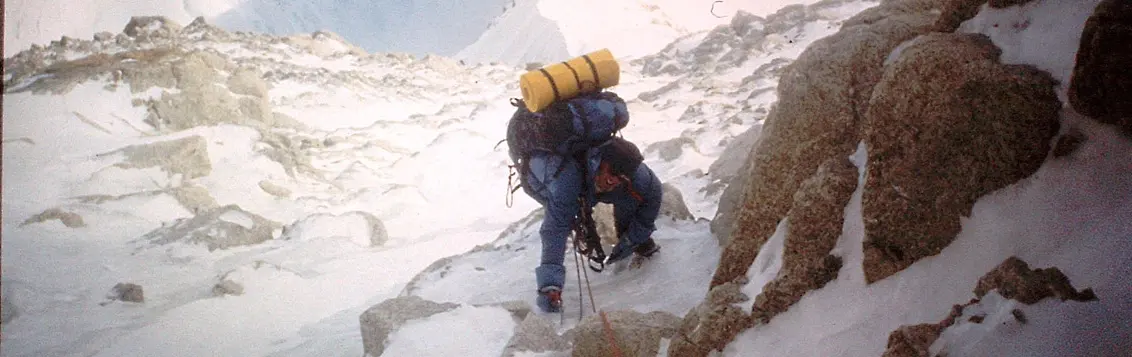 Een bergbeklimmer met een rugzak en uitrusting steekt met behulp van touwen een besneeuwde gletsjerspleet over op een gletsjer.