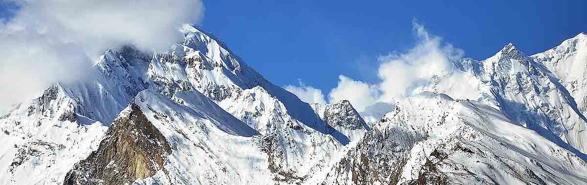 Met sneeuw bedekte bergtoppen onder een strakblauwe hemel, waarbij enkele wolken de hoogste top gedeeltelijk bedekken.