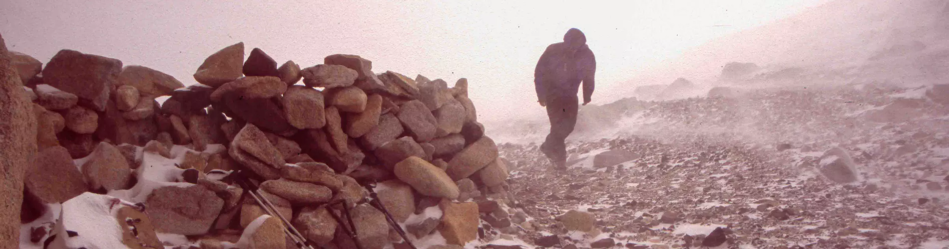Vier mensen in outdoorkleding staan op rotsachtige grond voor de iconische granieten torens van Torres del Paine in Chili, met sneeuwvlekken en een gletsjermeer aan de voet, onder een blauwe hemel.