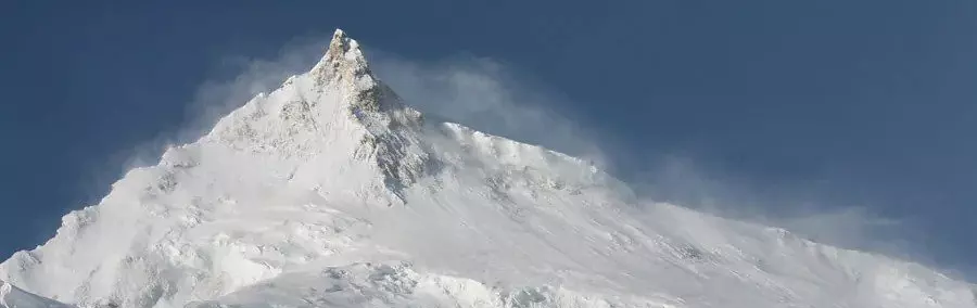 Twee bergbeklimmers in rode parka’s staan op een besneeuwde bergtop met een bordje van Kathmandu Expedition in hun handen, met achter hen een scherp afgetekende, met sneeuw bedekte top onder een helde