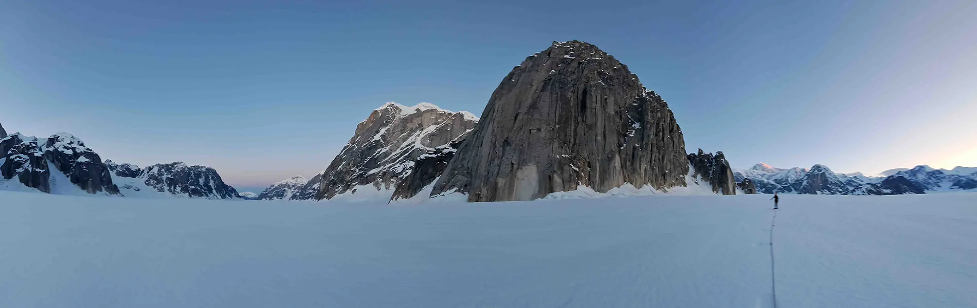 Uitzicht vanuit een gele tent die op een besneeuwde berghelling is opgezet, met uitzicht op ruige, met sneeuw bedekte bergtoppen en een vallei beneden, onder een gedeeltelijk bewolkte hemel.