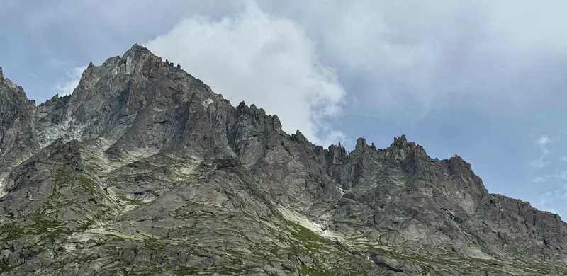 Een rotsachtige bergkam met grillige toppen onder een bewolkte hemel, met hier en daar groene begroeiing op de hellingen.