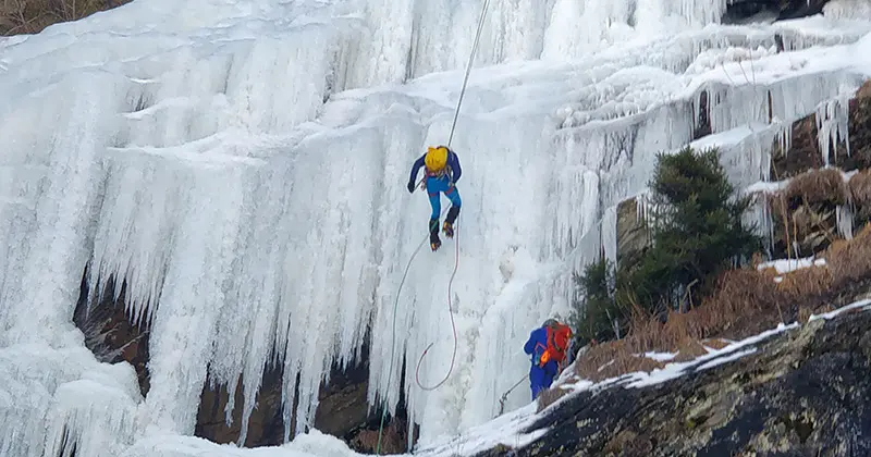 Een ijsklimmer die een bevroren waterval beklimt.